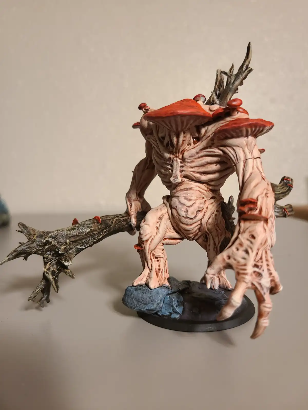 A highly detailed, painted miniature figurine depicts a grotesque humanoid creature with fleshy, wrinkled skin and large red…