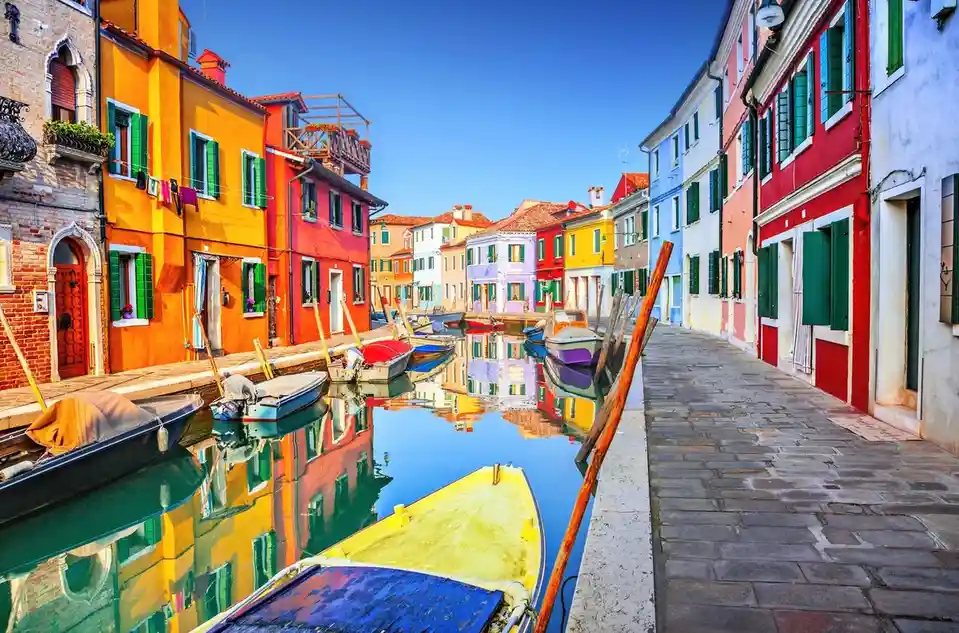 A vibrant, picturesque canal scene with colorful buildings lining both sides, their reflections mirrored in the calm water…
