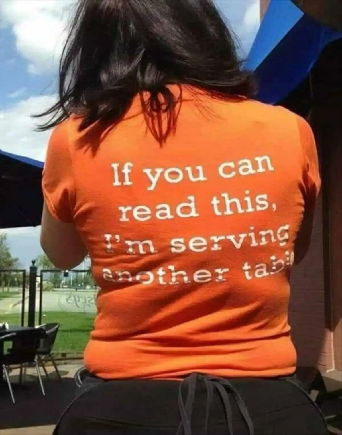 A person with dark hair is seen from behind, wearing an orange t-shirt with white text that reads 'If you can read this, I'm…