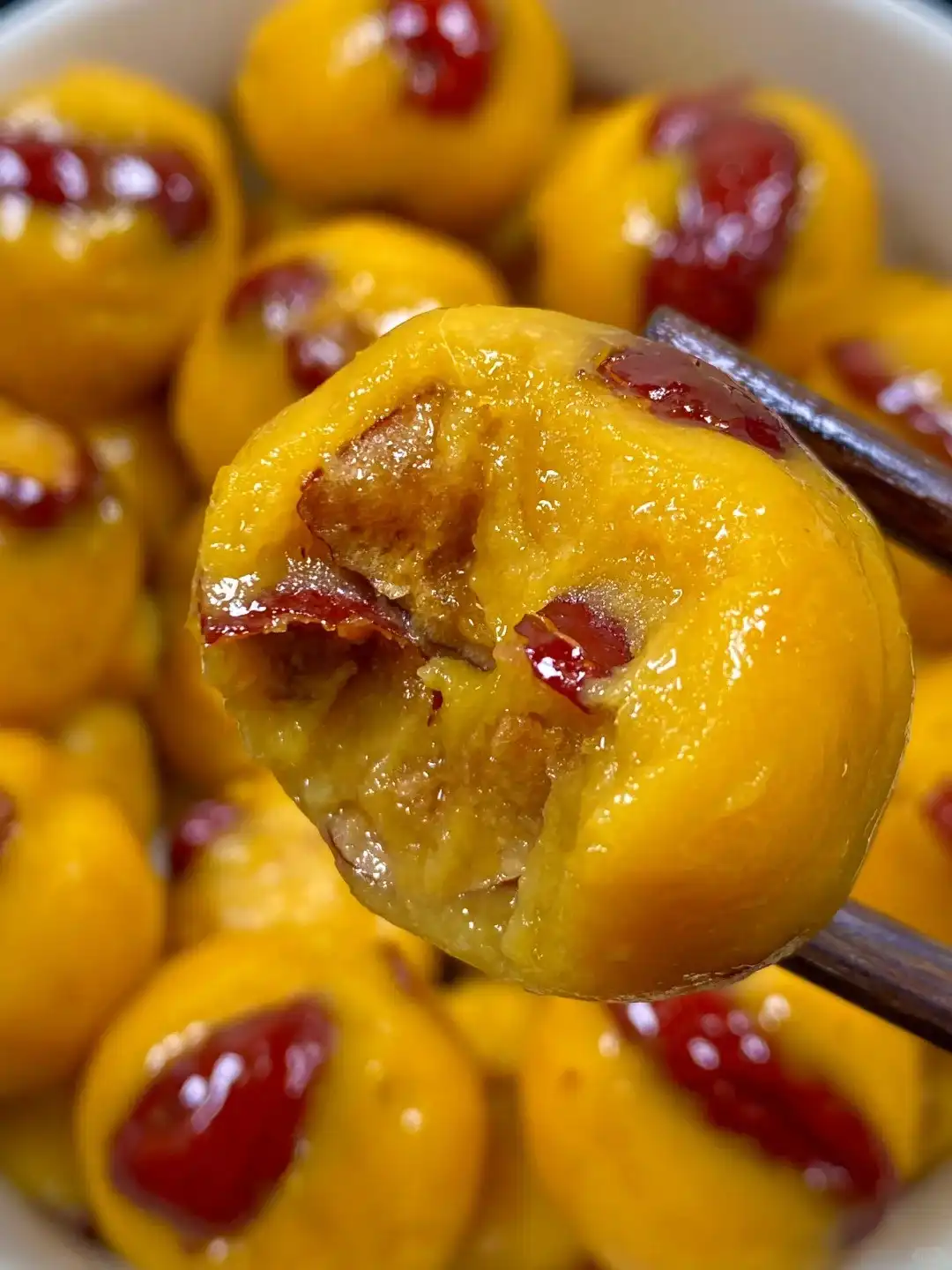 A close-up photo shows a pair of dark wooden chopsticks holding a steamed, golden-yellow dumpling that has been bitten into…