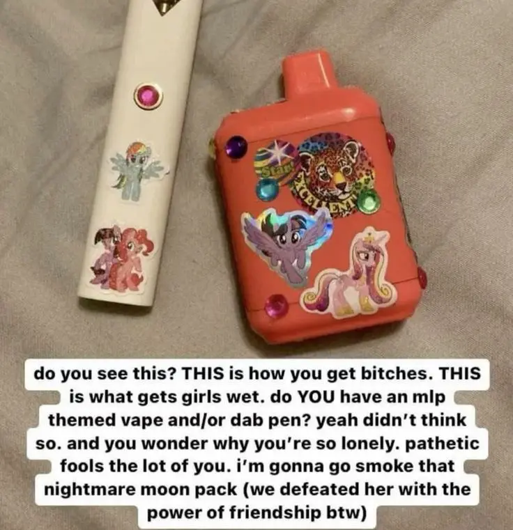 Two vape pens, one white and one orange, are covered in My Little Pony stickers and gems, lying on a gray fabric surface…