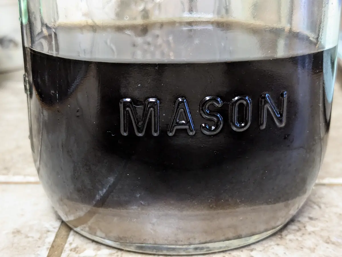 A close-up photo shows a glass mason jar filled with dark coffee, with the word 'MASON' embossed on its side. The coffee has…