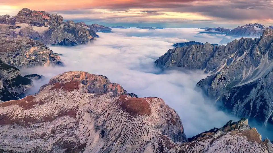 Tre Cime di Lavaredo National Park in northeastern Italy is shrouded in fog, showcasing the rugged Dolomite mountains named…