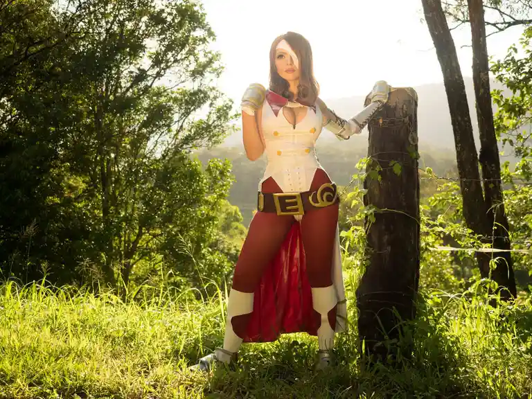 A person in a detailed cosplay of a female video game character with a white eye patch stands outdoors in a grassy, wooded…
