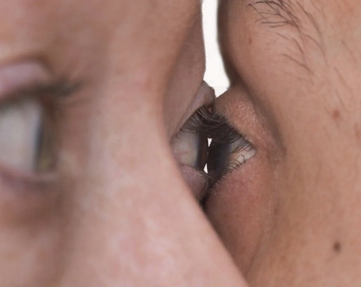 A close-up photo shows two people's faces pressed together, with one person's eye visible and the other's face blurred in…
