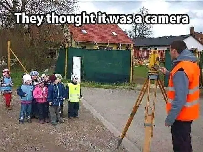 A group of young children in winter hats and jackets stand in a line, looking curiously at a man in an orange safety vest…