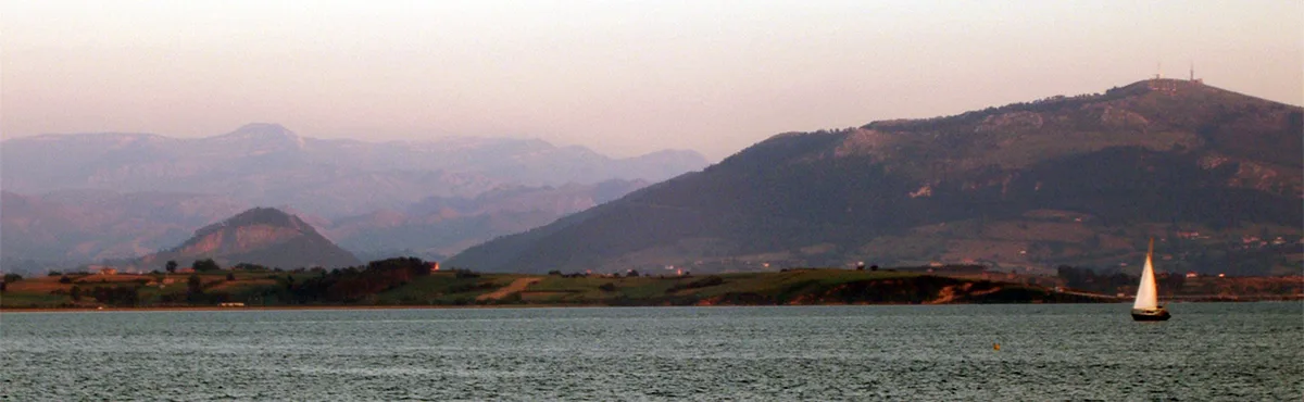 A serene landscape photo of a sailboat on a calm body of water with rolling hills and mountains in the background under a…