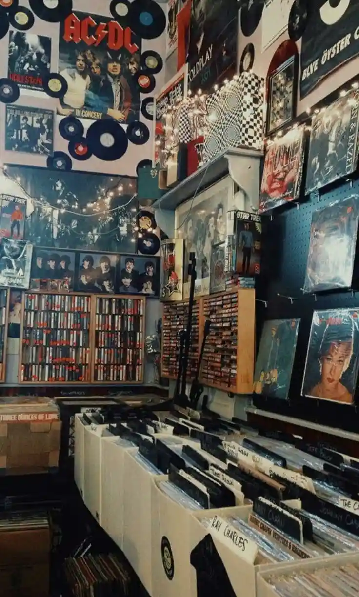 A cozy, cluttered record store filled with shelves of vinyl records, posters of bands like AC/DC and Coldplay, and string…