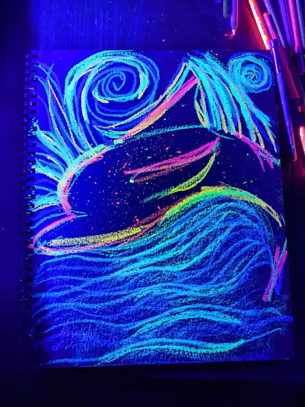 A spiral-bound notebook lies under blacklight, revealing a vibrant fluorescent drawing of a stylized face with swirling hair…
