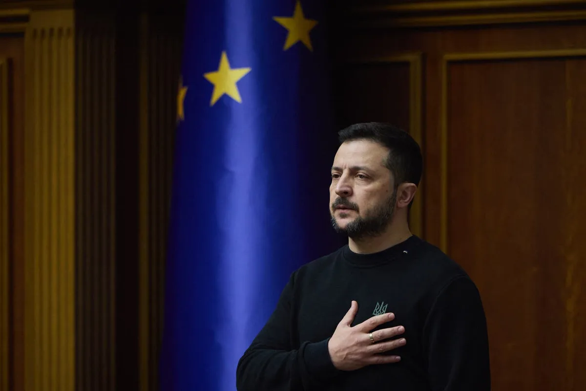 a man with a beard and dark hair, wearing a black sweatshirt with a small green emblem, stands with his right hand over his…