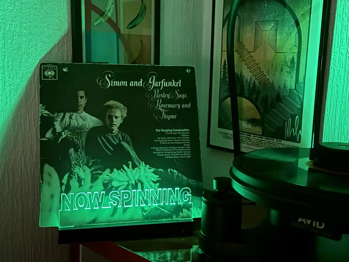 A green-tinted photo shows a vinyl record album cover for Simon and Garfunkel's 'Parsley, Sage, Rosemary and Thyme' standing…