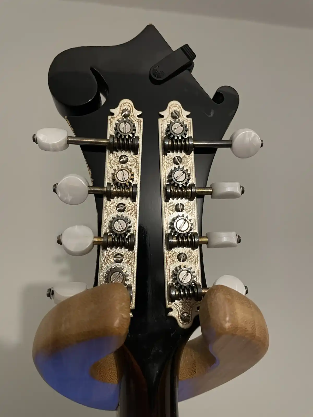 A close-up photo of a black guitar headstock with ornate, gear-like tuning pegs and white tuning knobs, overlaid with the…