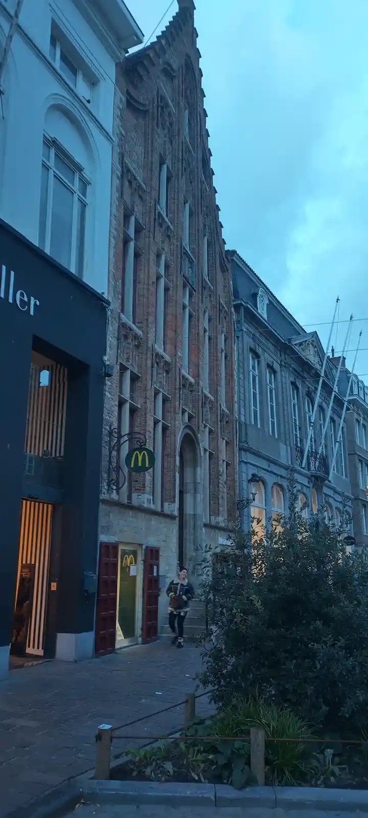 A person walks past a historic, ornate brick building with a McDonald's sign hanging from its facade, contrasting the old…