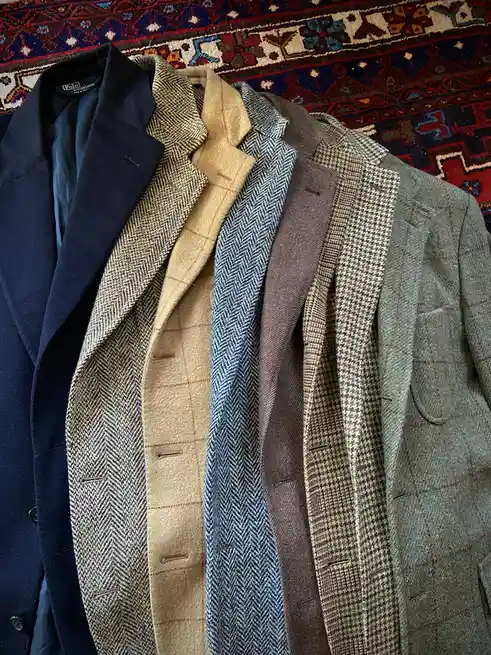 A close-up shot shows six men's jackets hanging side-by-side on a colorful patterned rug, displaying various textures and…