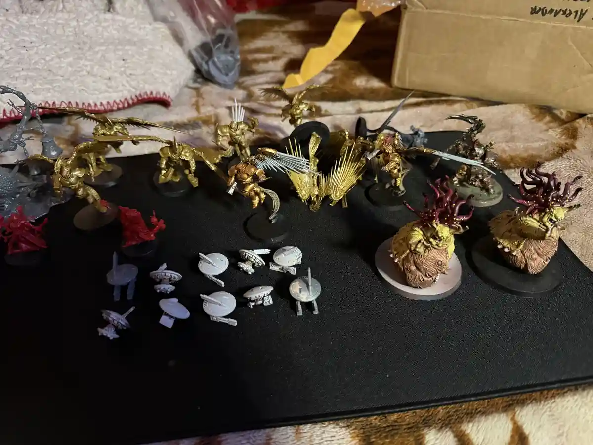 A collection of painted miniature figurines, mostly in gold, arranged on a black mat, with some unpainted grey and red…
