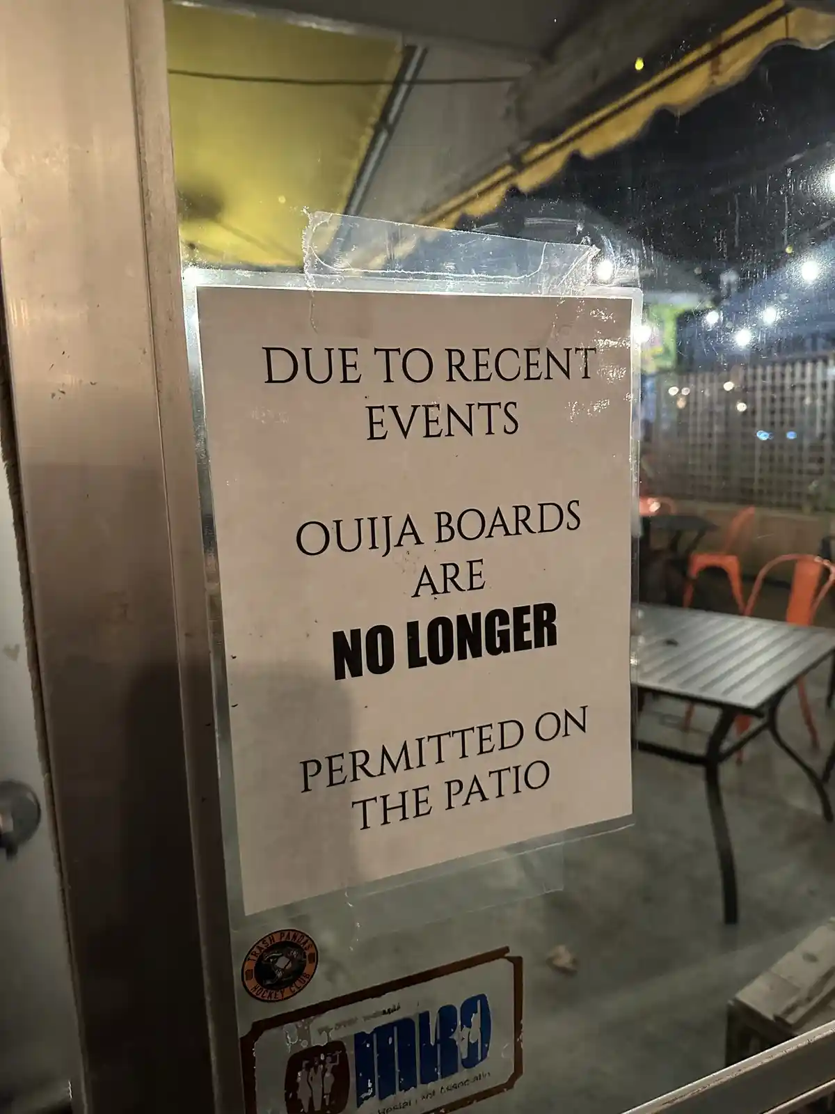A sign taped to a glass door or window reads 'DUE TO RECENT EVENTS OUIJA BOARDS ARE NO LONGER PERMITTED ON THE PATIO'…