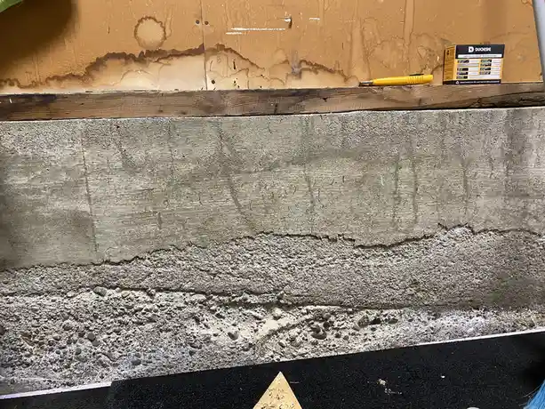 A close-up photo shows a weathered concrete wall with a wooden beam above it, a yellow utility knife, and a small box of…