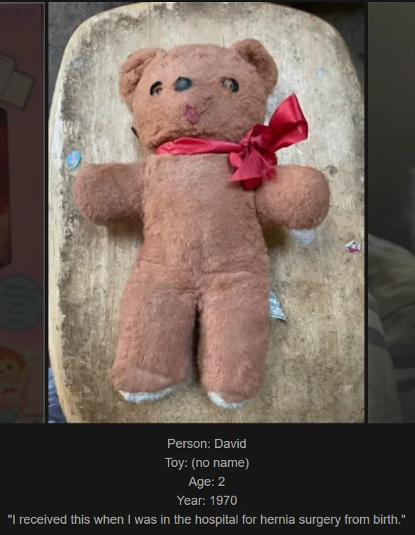 A brown, worn stuffed teddy bear with a red bow lies flat on a wooden surface. The bear has visible stitching, faded fur…