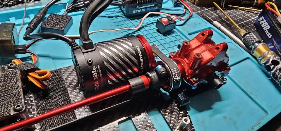 A close-up photo of a red and black hobbywing ezrun 3652 motor mounted on a carbon fiber chassis, surrounded by tools and…