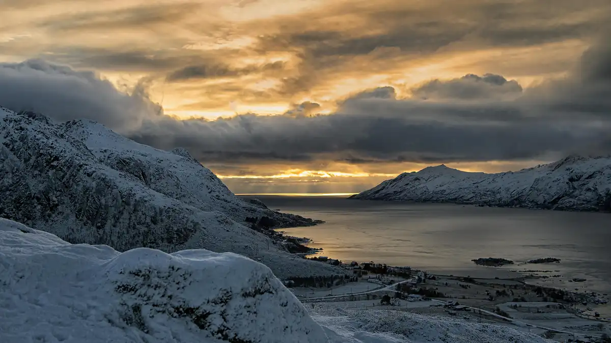 Dramatic clouds cascade across the frozen fjord, their wispy tendrils tangled with the snow-covered peaks of Lofoten's…