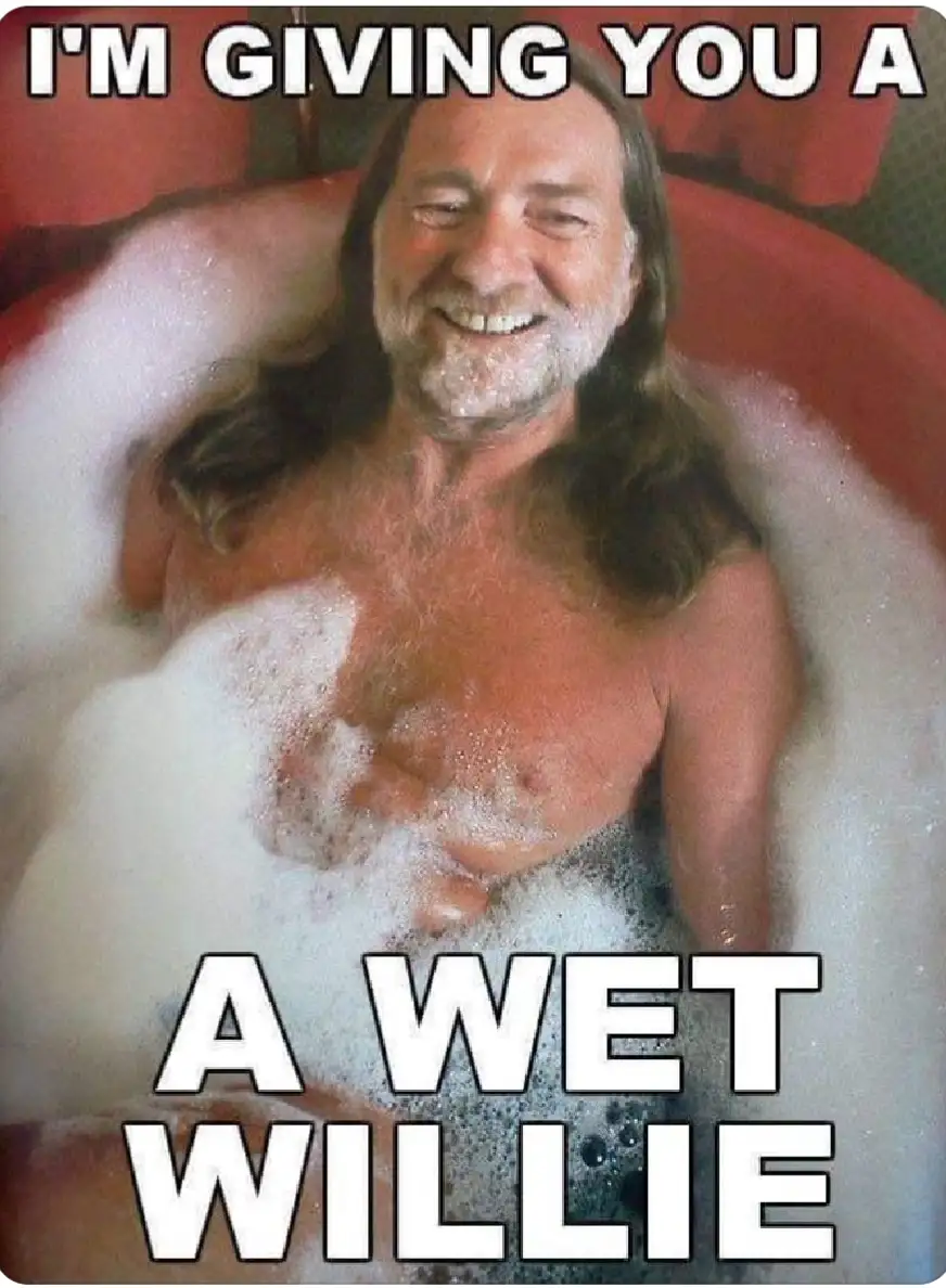 A man with long hair and a beard is smiling while soaking in a bubble bath filled with white foam. The text overlaid on the…