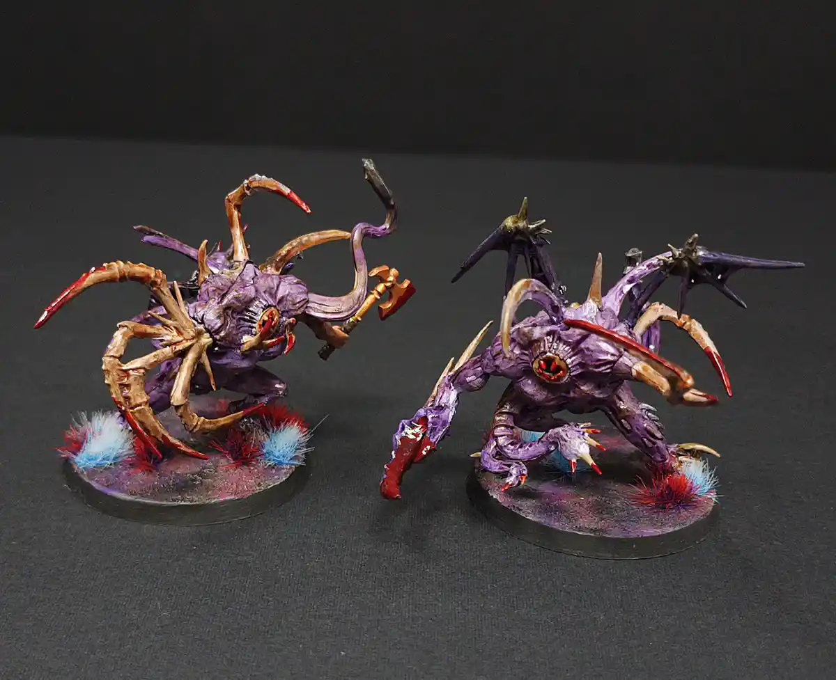 Two intricately painted purple and bone-colored fantasy monster miniatures stand on circular bases with red and blue fuzzy…