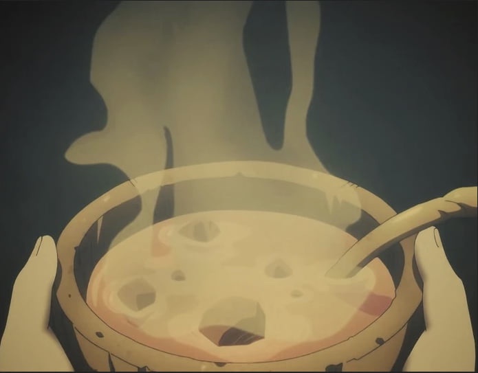 A pair of hands holds a steaming bowl of soup, with a spoon resting inside. The bowl has a cracked, uneven surface. The…