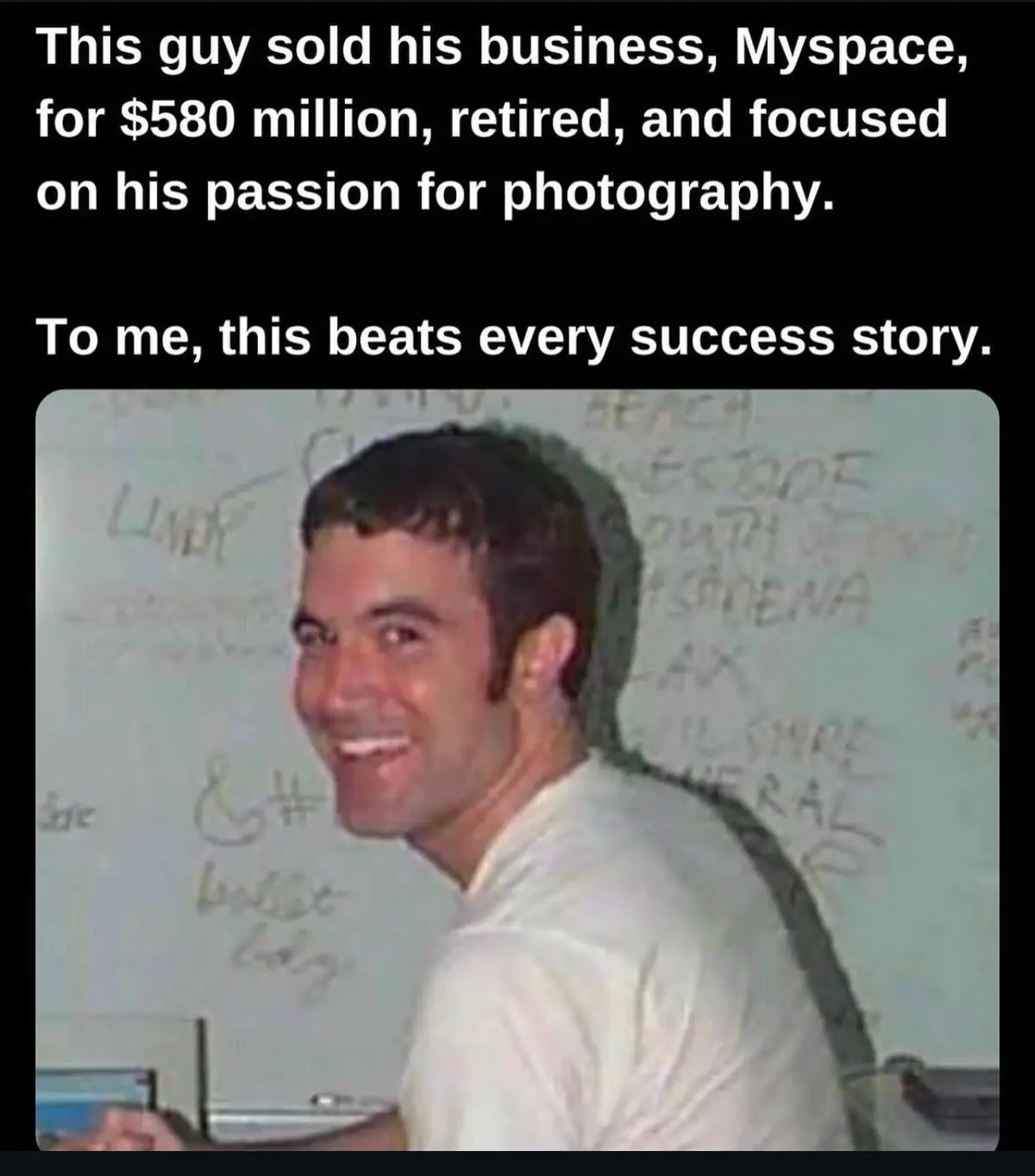 A man in a white shirt smiles while looking over his shoulder at the camera, standing in front of a whiteboard covered in…