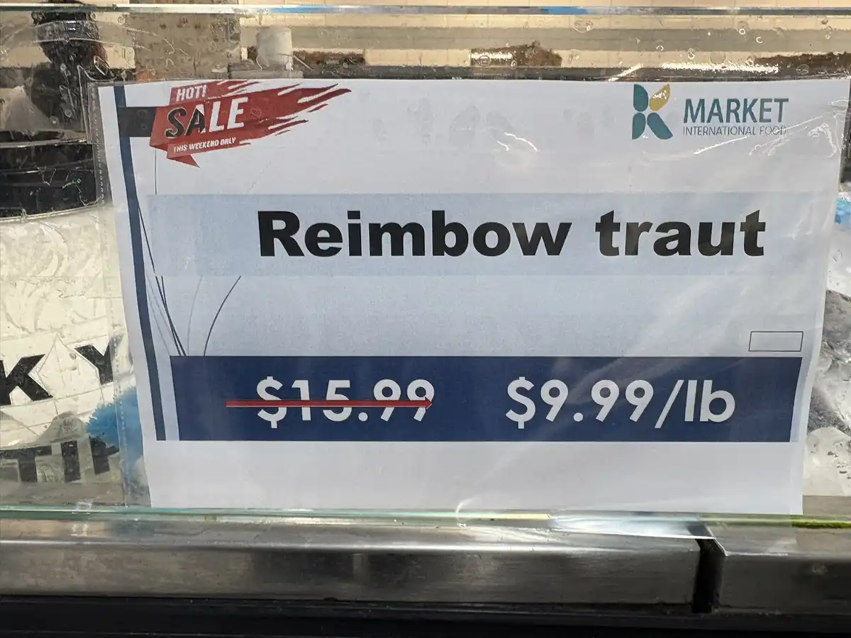 A price sign at a market advertises 'Reimbaw traut' for $9.99/lb, down from $15.99, with a 'HOT! SALE THIS WEEKEND ONLY'…