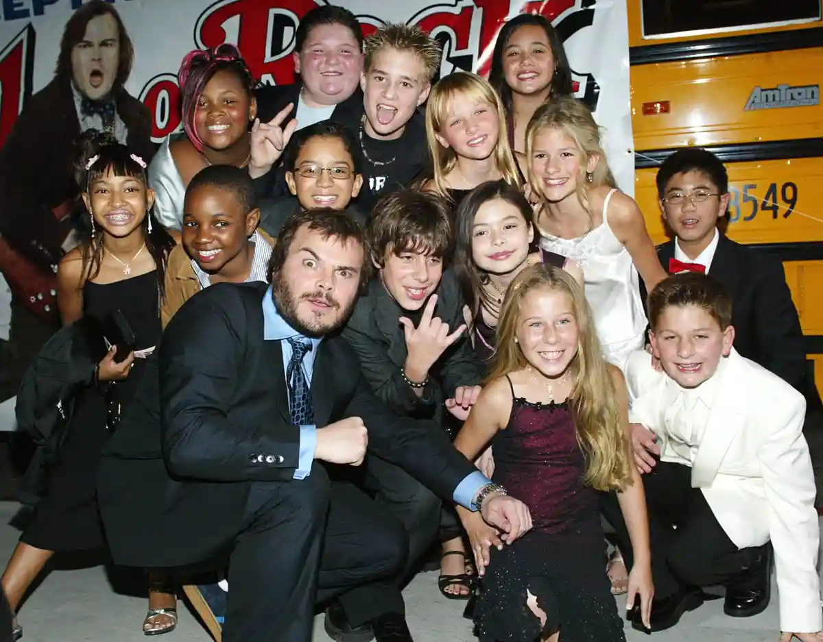jack black, in a suit, poses with a group of children at what appears to be a school event or convention, with a yellow…