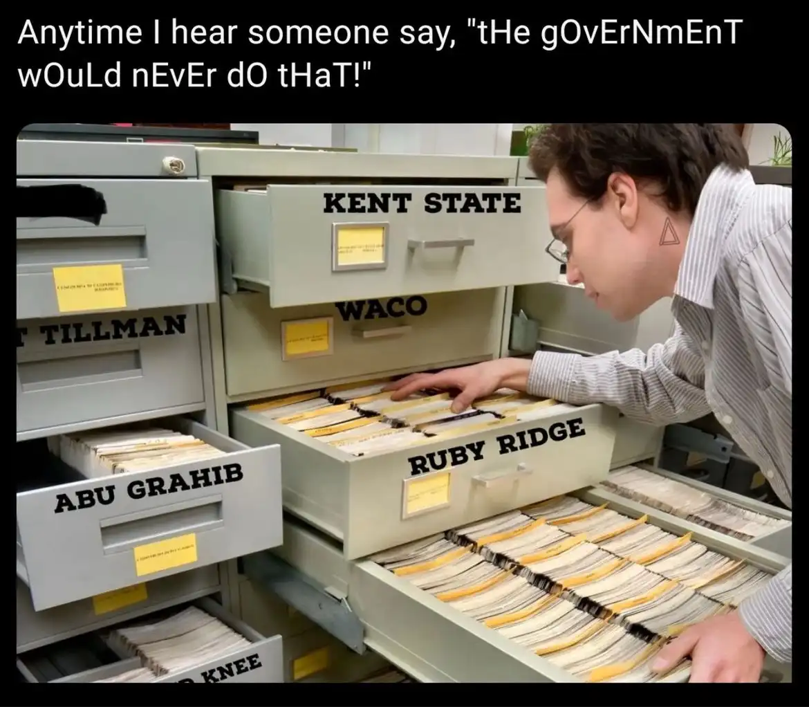 A person in a striped shirt and glasses is looking through open filing cabinet drawers labeled with names of historical…