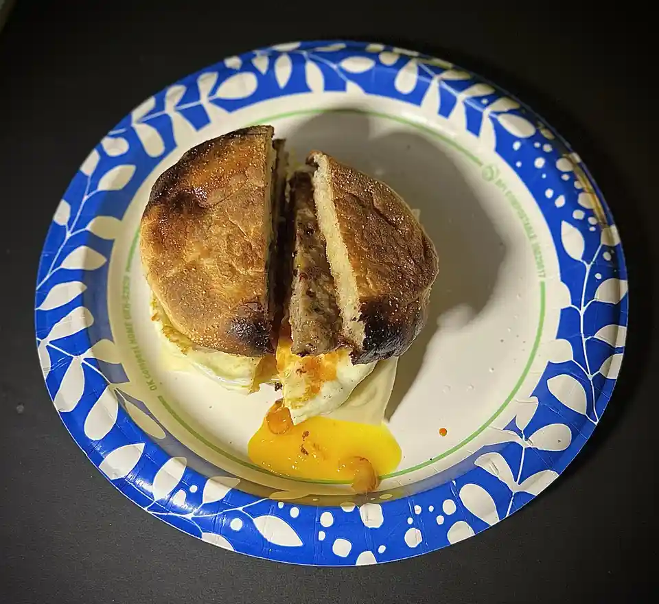 A sandwich, cut in half and sitting on a blue and white patterned paper plate, has its filling—likely egg and…