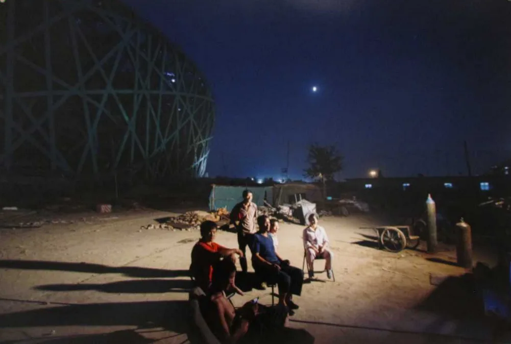 A nighttime photo shows five men sitting and standing in a dirt lot under a starry sky, with a large, illuminated geodesic…