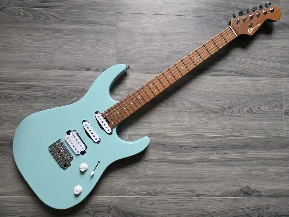 A light blue electric guitar with a wooden neck and fretboard lies diagonally on a gray wood-patterned floor. The guitar has…