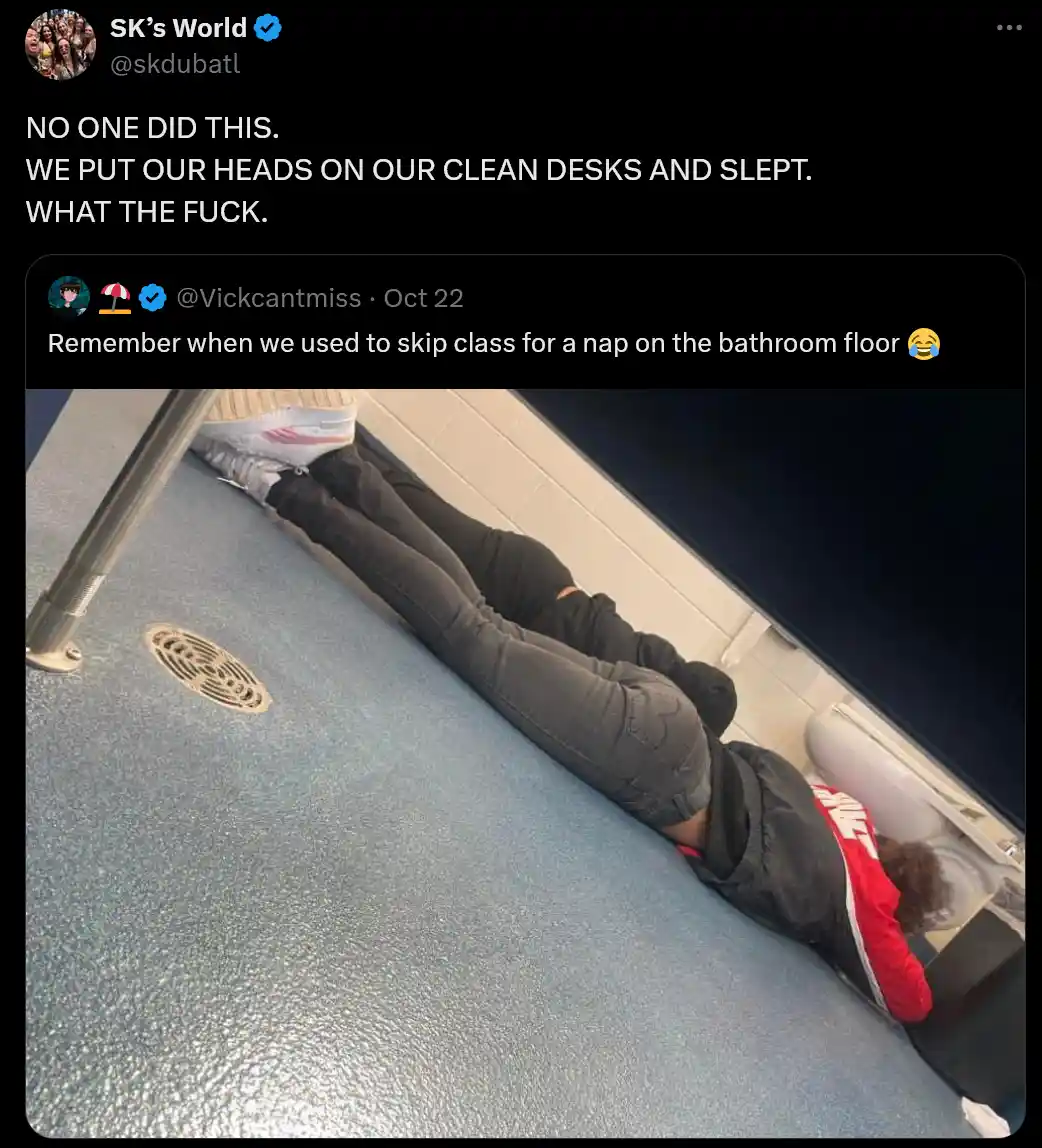 A person is lying face down on a blue school floor, head resting on a clean desk, with their legs extended. The overlaid…