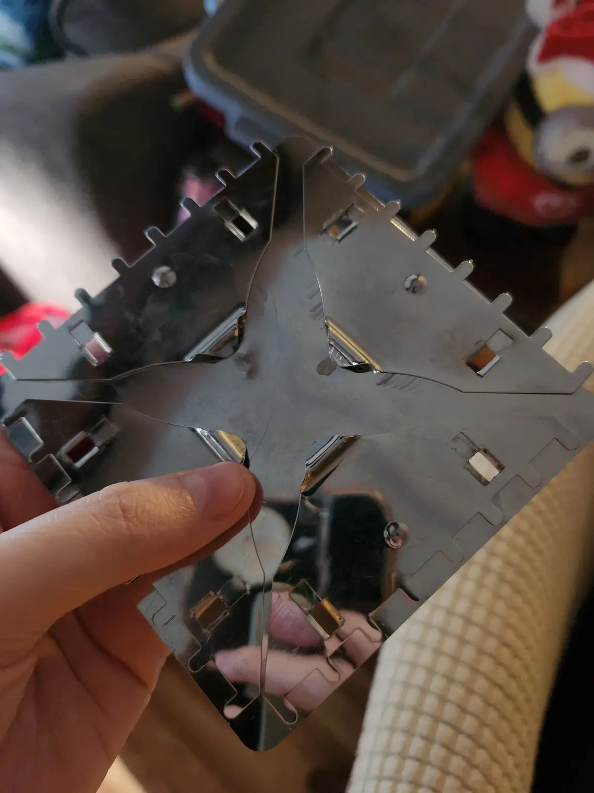 A hand holds a shiny, broken metal phone charging port bracket, which is cracked down the middle and reflects the person…