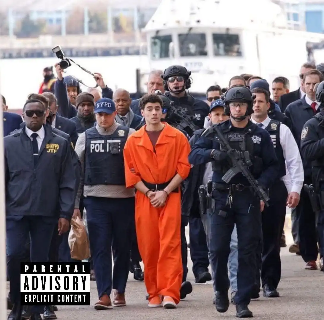 A young man in an orange prison jumpsuit is being escorted by multiple NYPD officers, some in tactical gear with rifles, on…