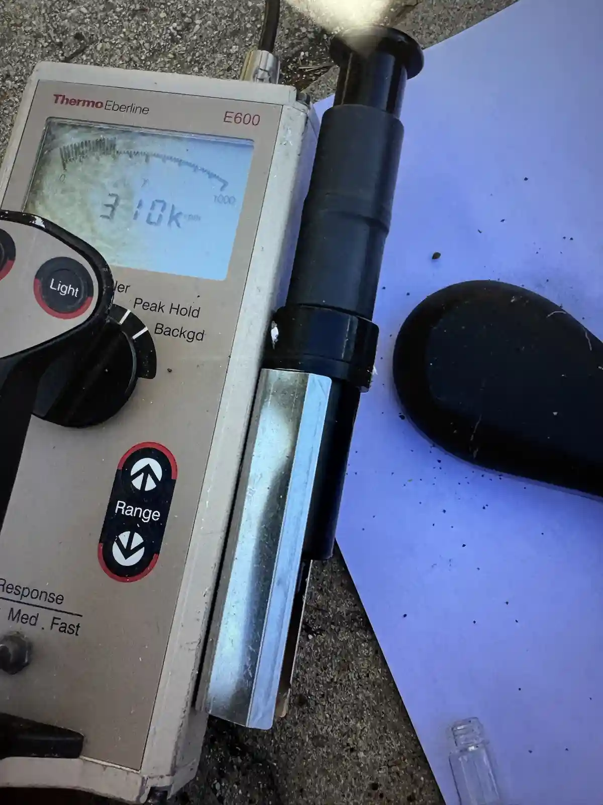 A close-up photo shows a beige Thermo Eberline E600 radiation detector with a digital display reading '310k rpm'. The device…