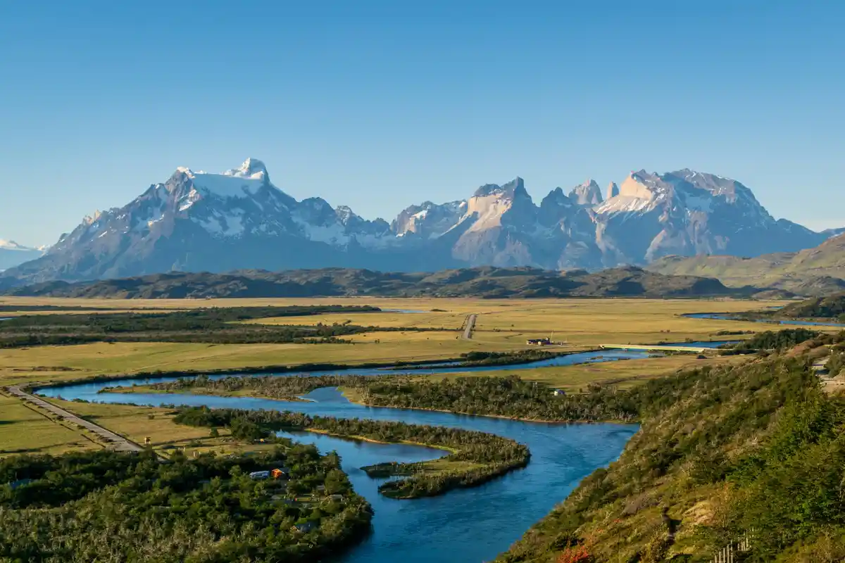 A scenic landscape photo shows a winding river flowing through green plains with snow-capped mountains in the background…