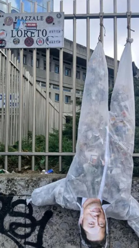 A man's head is photoshopped onto a plastic bag hanging from a metal fence, with a sign reading 'PIAZZALE LORETO' visible…