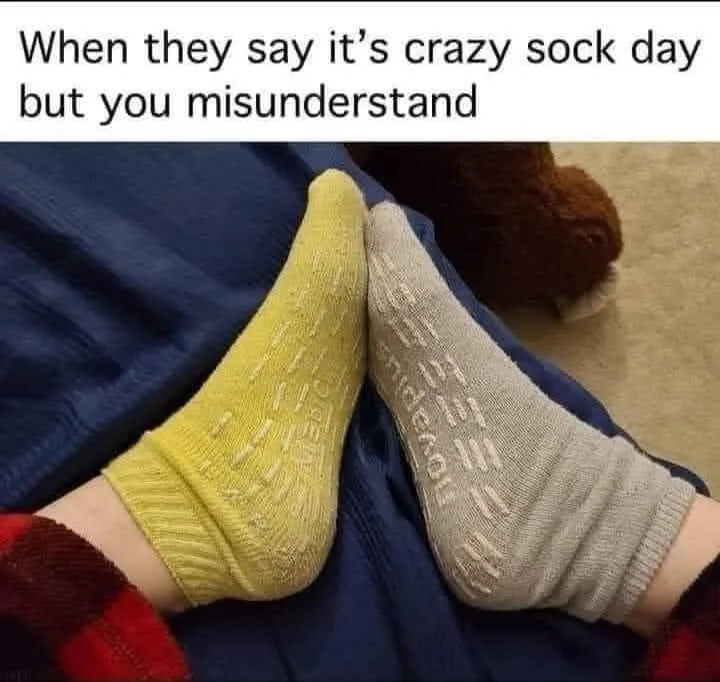A close-up photo shows two mismatched socks, one yellow and one gray, worn on feet resting on a blue blanket. The yellow…