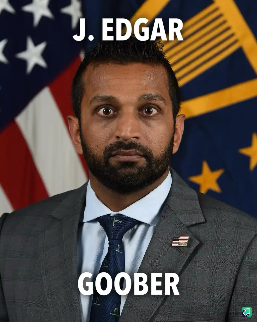 A man in a gray suit, light blue shirt, and patterned tie stands in front of an American flag and a blue flag with yellow…