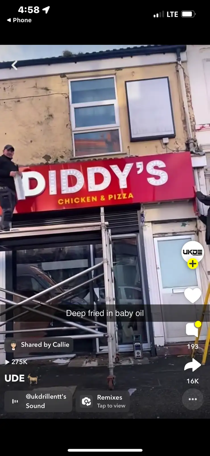 Two men are installing a red sign that reads 'DIDDY'S CHICKEN & PIZZA' on a storefront with scaffolding. A text overlay…