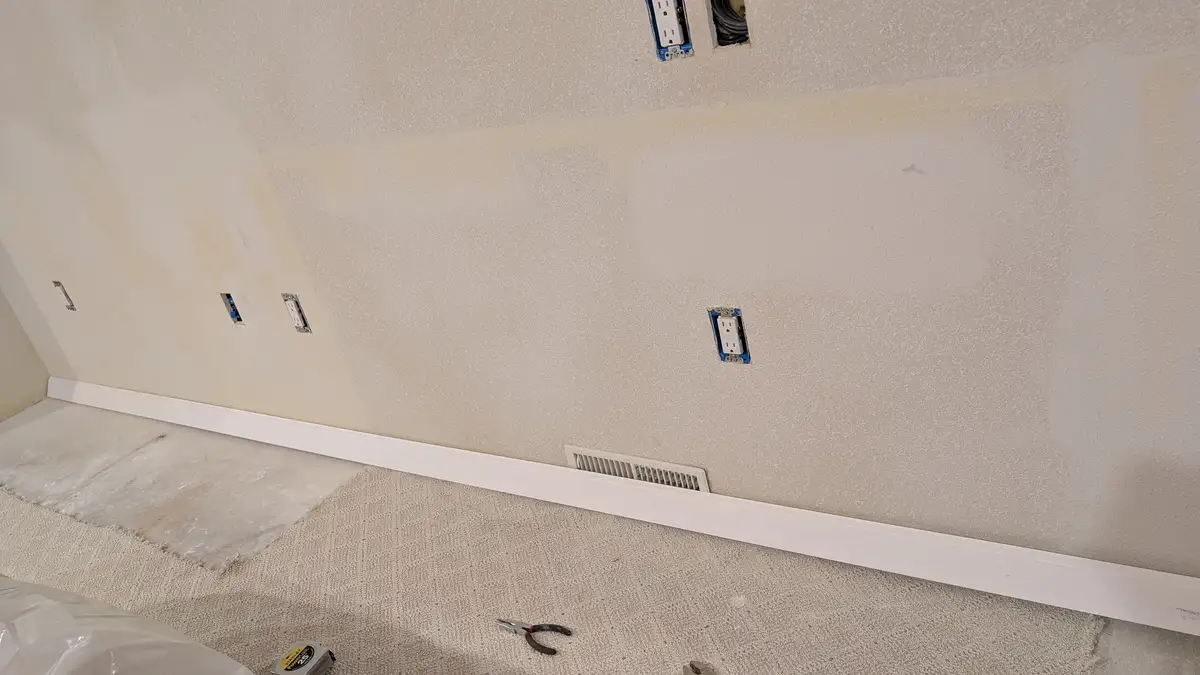 A room under renovation shows a wall with multiple electrical outlets, some with blue covers and others exposed, set against…