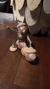 A small wooden figurine of a squirrel sitting on a wooden floor, holding an acorn in one hand and gesturing with the other…
