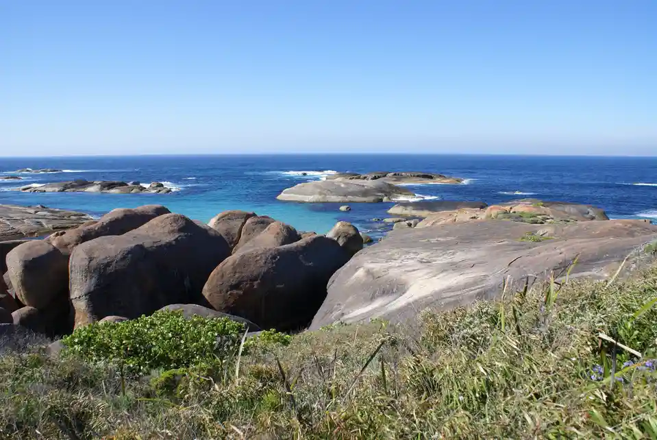A scenic coastal photo shows large, rounded boulders in the foreground with turquoise and deep blue ocean water behind them…