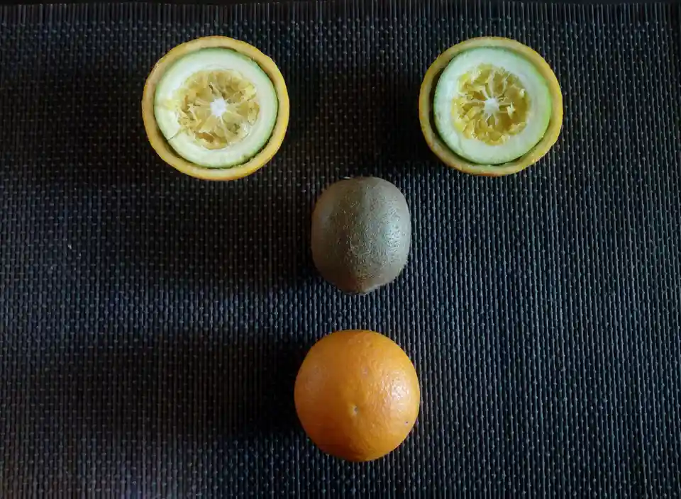 An overhead photo shows three fruits arranged on a dark textured mat: two halves of a citrus fruit (likely a kumquat or…