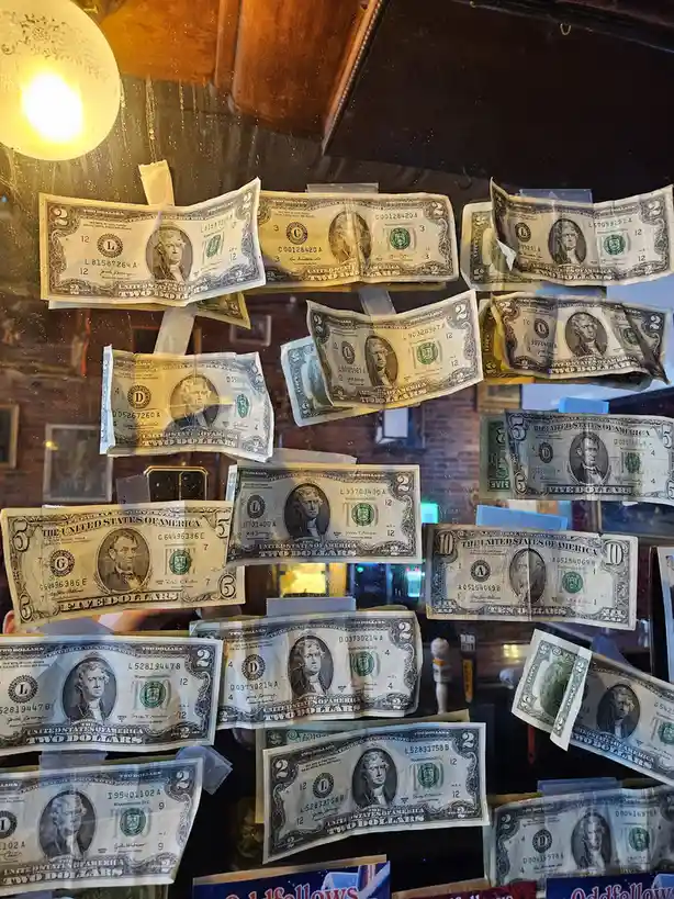 A window is covered with numerous US dollar bills of various denominations, mostly two-dollar bills, taped haphazardly…