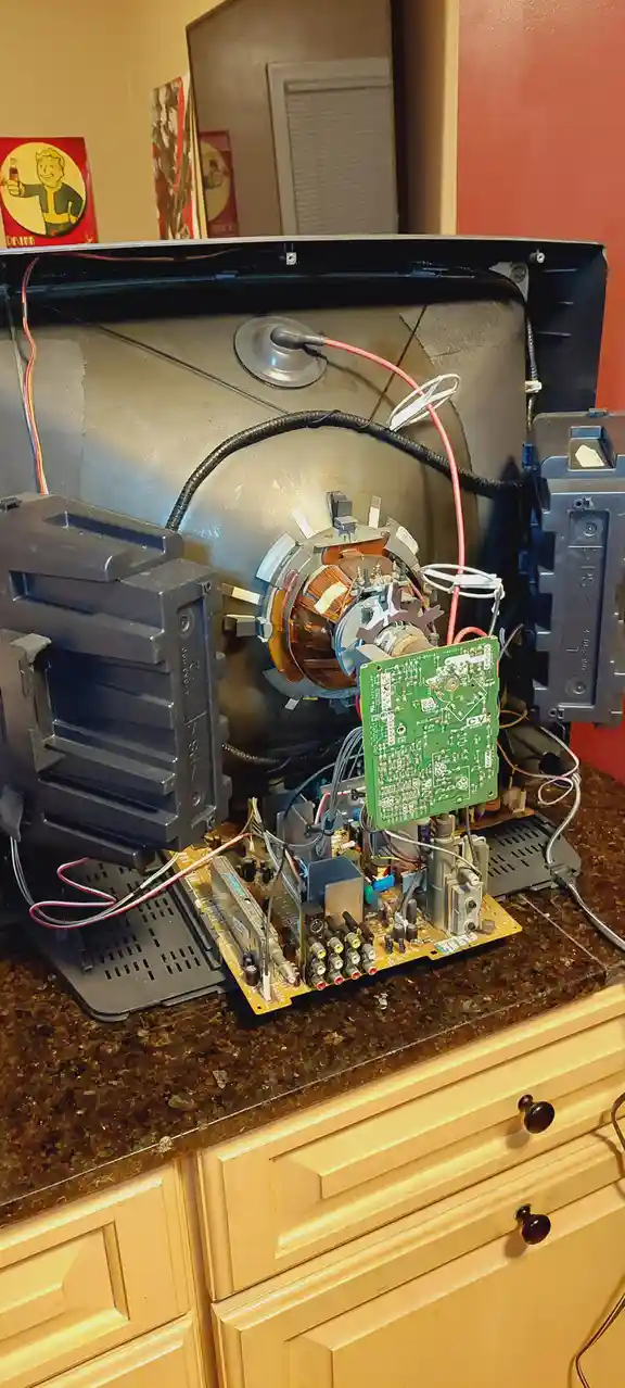 A disassembled CRT television sits on a kitchen counter, its internal components exposed, including a large cathode-ray…