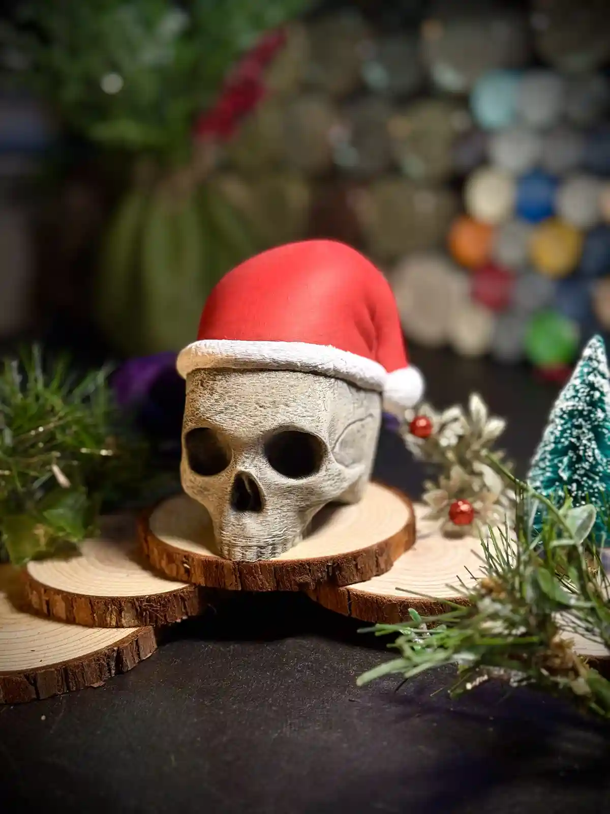 A decorative skull wearing a red Santa hat sits atop stacked wooden slices, surrounded by Christmas greenery and a small…